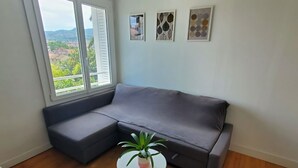 Habitació d'angle amb un sofà seccional gris, una taula blanca petita amb una planta i dos quadres amb marc a la paret.