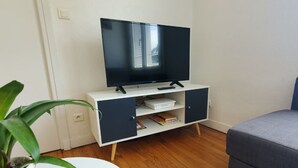 Habitació amb un suport de televisió blanc i negre, un sofà gris, una taula rodona blanca i una planta en test.