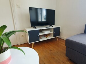 Ein Zimmer mit einem weißen und schwarzen Fernsehschrank, einem grauen Sofa, einem runden weißen Tisch und einer Topfpflanze.