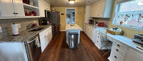 Una cocina con alacenas blancas, un refrigerador de acero inoxidable, un lavamanos y un ventanal con vistas.