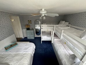 Un dormitorio con literas, ventilador de techo, cómoda, espejo y papel tapiz estampado.