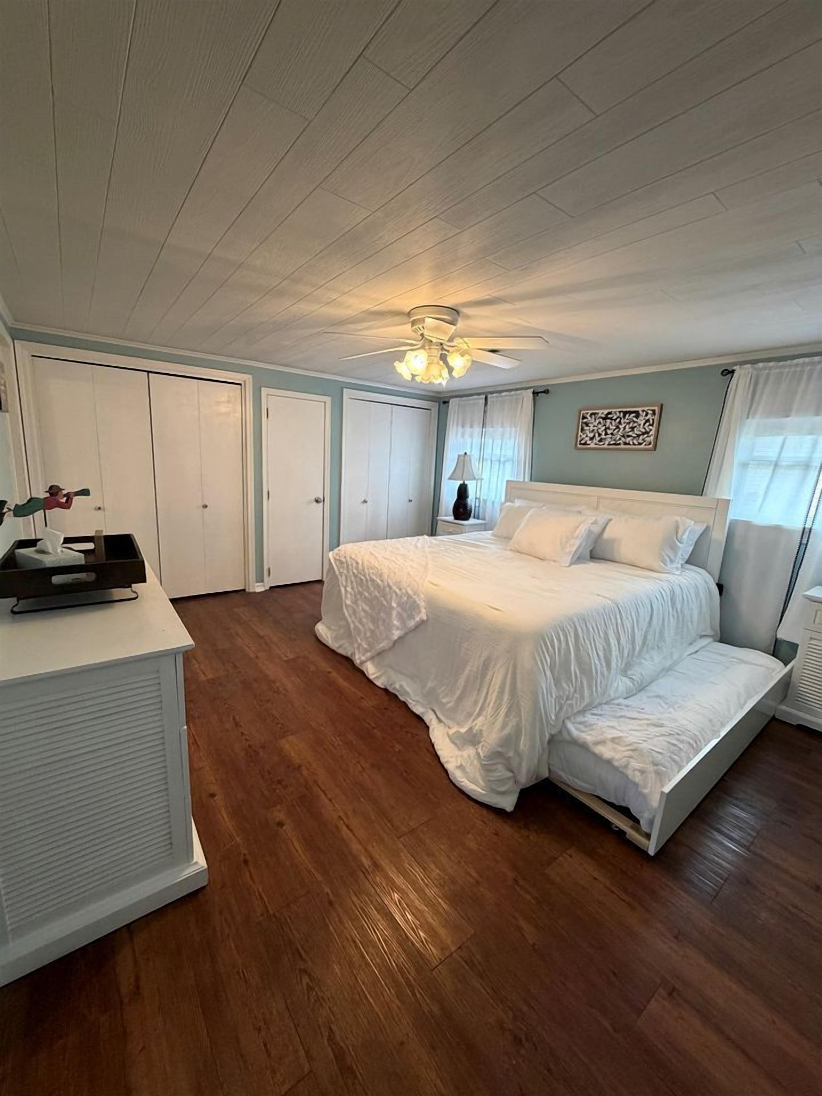 A bedroom with a bed, a desk, a ceiling fan, and a nightstand.