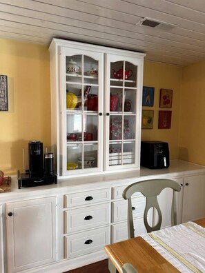 Eine Küche mit einem weißen Schrank, einer Kaffeemaschine und einem Stuhl.