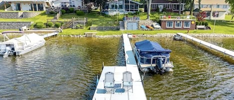 Un muelle con barcos, un área techada y casas al fondo.