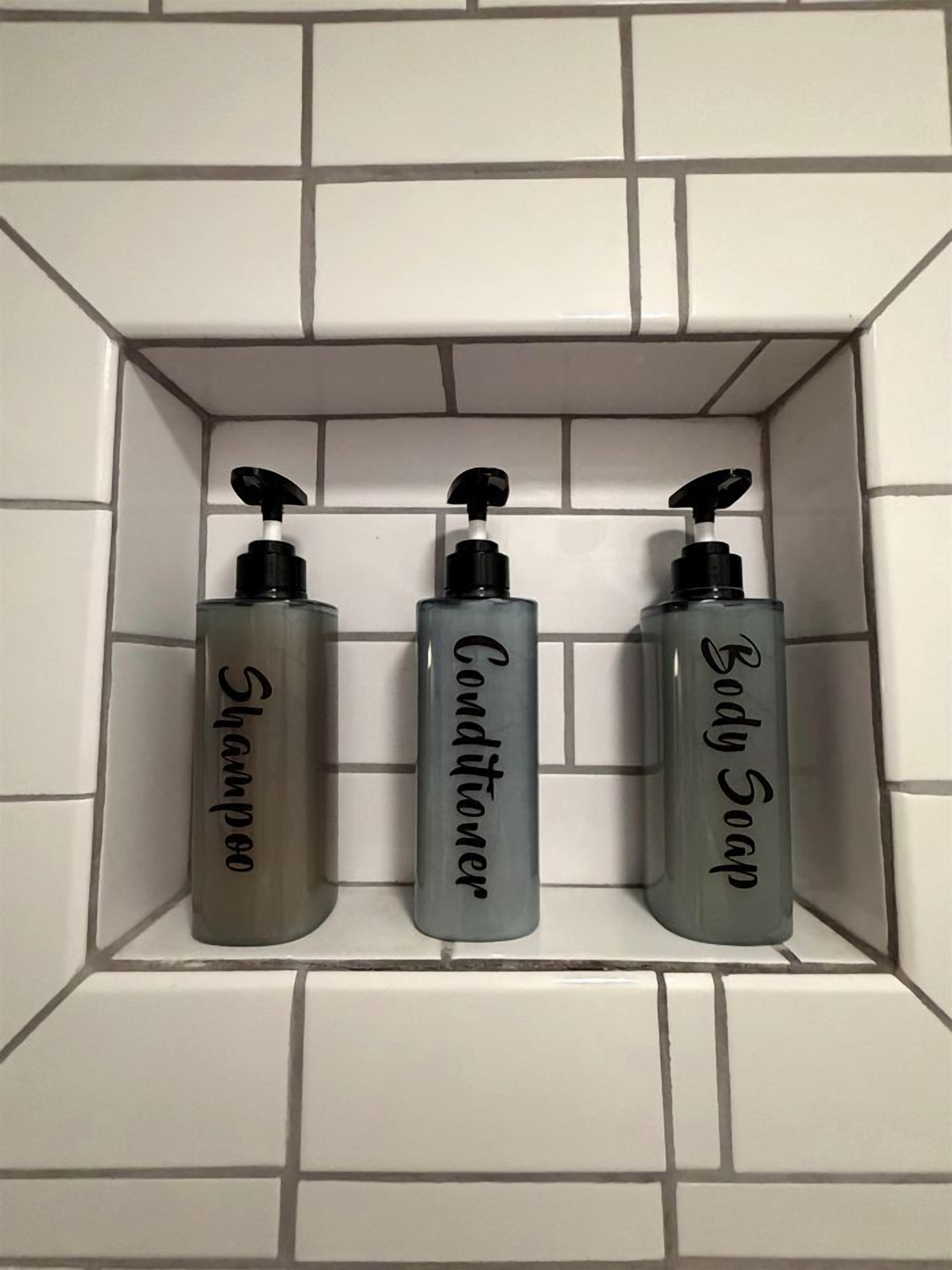 Trois bouteilles de shampoing, d’après-shampoing et de savon pour le corps, posées sur une étagère carrelée dans la salle de bain.