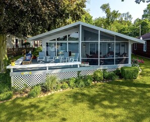A modern glass house with a deck, surrounded by a white fence and greenery. - Cozy Lakefront Cabin with Pontoon and Paddleboards Near Fremont, Indiana (Fremont)