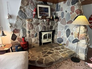 Una chimenea de piedra con un estufa de leña blanca, un tanque de gas rojo y un cuadro enmarcado encima.