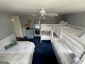 Un dormitorio con literas, ventilador de techo, cómoda, espejo y papel tapiz estampado.