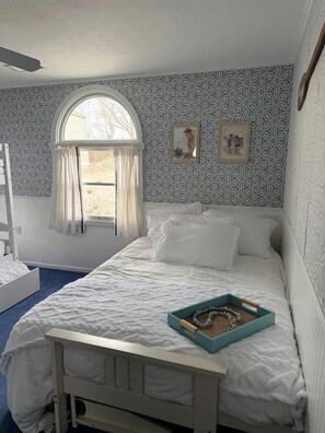 A bedroom with a bed, a window with curtains, a wall with a pattern, and a small table with a tray.