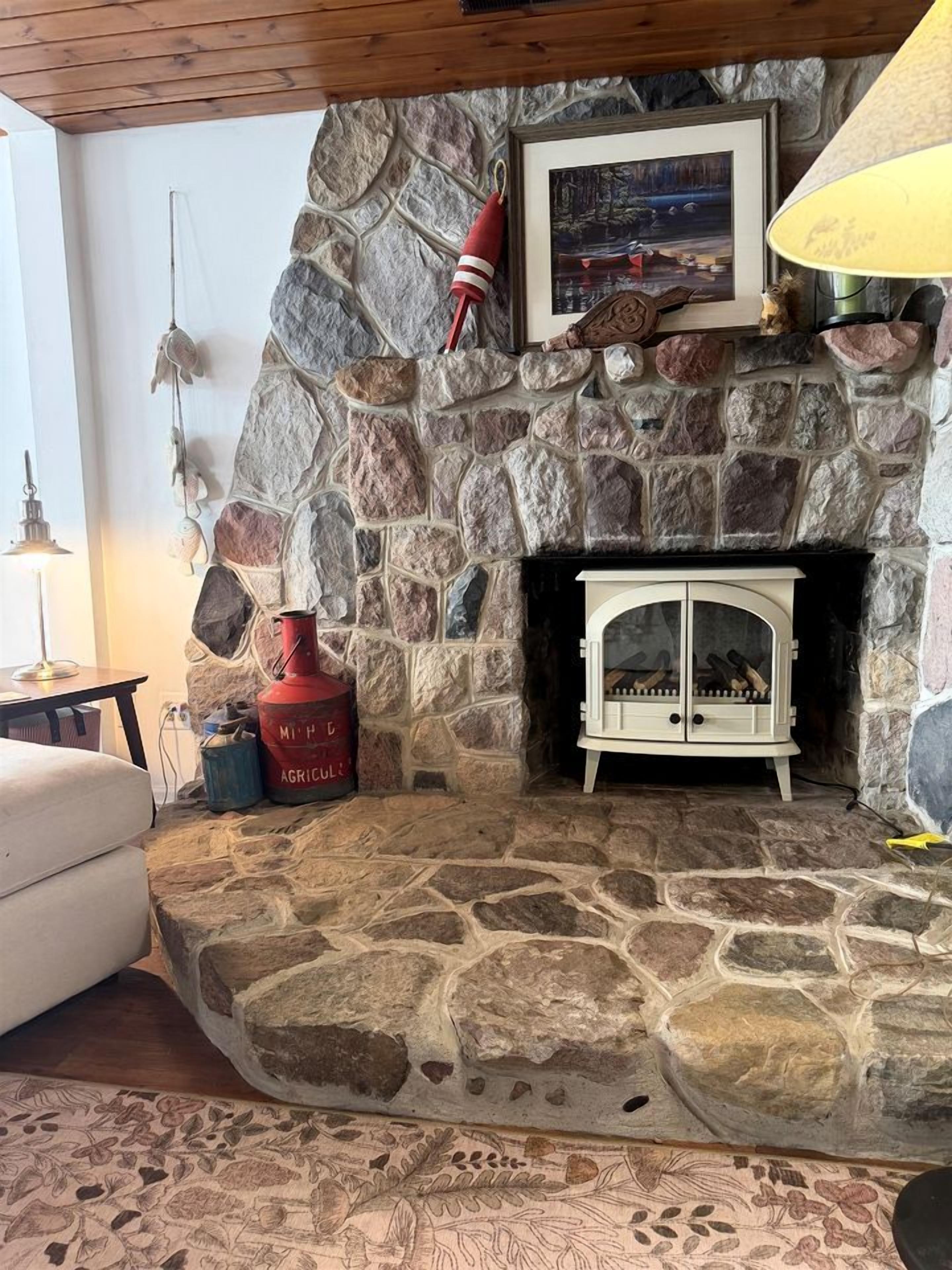 Une cheminée en pierre avec un meuble blanc, une bouteille de gaz rouge et un tableau encadré au-dessus.