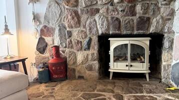 Une cheminée en pierre avec un meuble blanc, une bouteille de gaz rouge et un tableau encadré au-dessus.