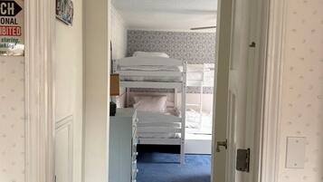 A narrow hallway leading to a room with a bunk bed, a patterned wall, and a blue carpet.