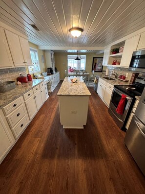 A kitchen with wooden floors, white cabinets, a central island, stainless steel appliances, and a pendant light.