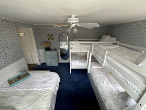 A bedroom with bunk beds, a ceiling fan, a dresser, a mirror, and patterned wallpaper.