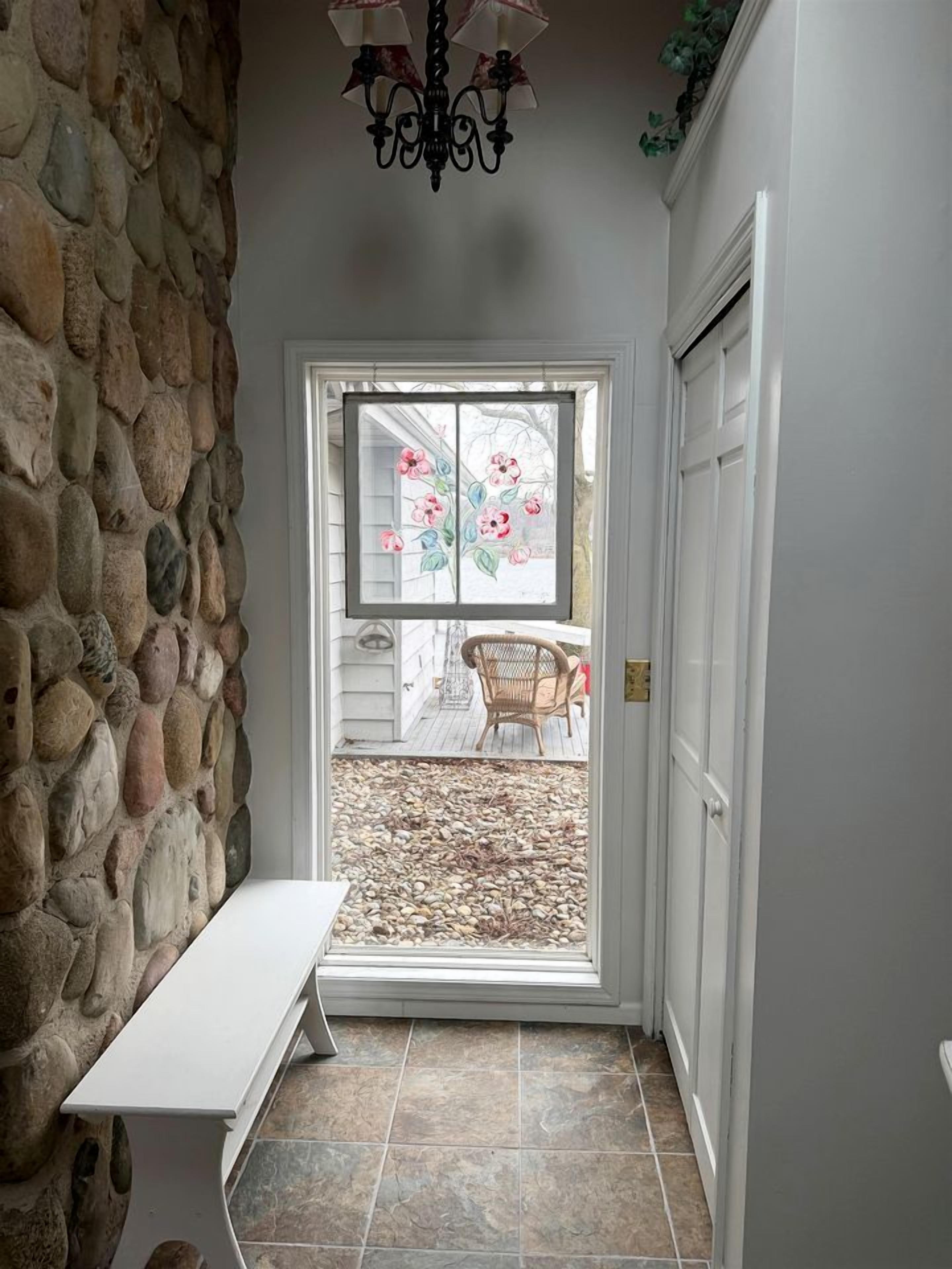 A stone wall, a bench, a door with a glass panel, and a view of a patio with chairs.
