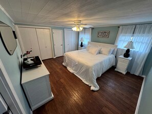 Une chambre à coucher comprenant un lit, des tables de chevet, un radiateur, un ventilateur de plafond et une fenêtre avec des rideaux.