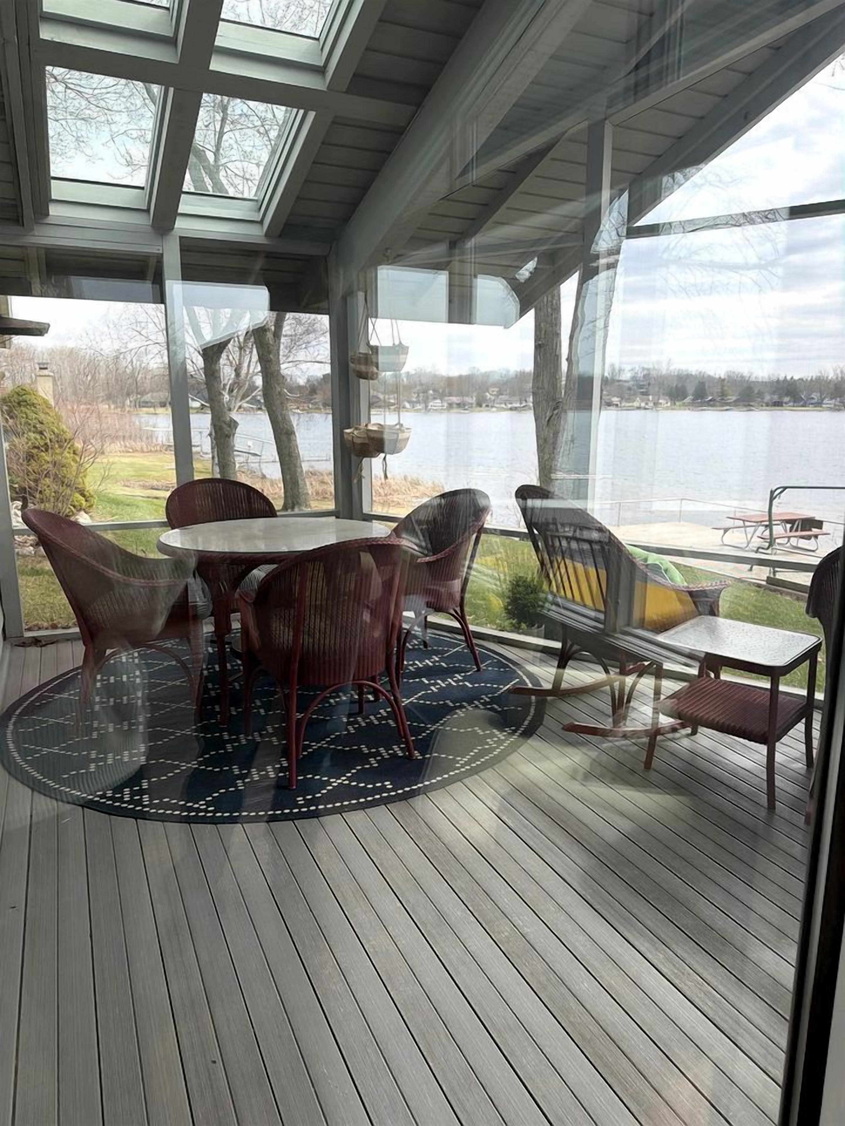 A covered outdoor deck with a table and chairs, overlooking a body of water.