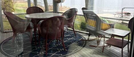 A covered outdoor deck with a table and chairs, overlooking a body of water.
