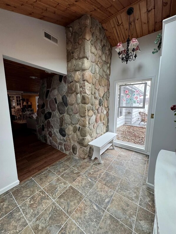 A stone wall, a bench, a chandelier, and a view through a glass door.