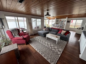A cozy living room with a sofa, armchair, and coffee table, large windows with a view of a lake, and wooden flooring.