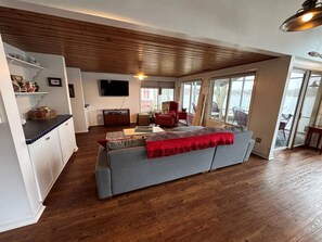Un vaste espace de vie comprenant un canapé, un plancher en bois et une grande fenêtre donnant sur un paysage agréable.