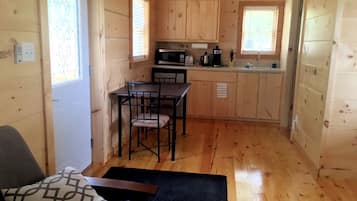 A compact wooden cabin with a kitchenette, a dining area, and a single bed.