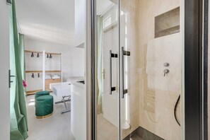 Ein modernes Badezimmer mit einer Duschkabine aus Glas, einem weißen Waschbecken und einem grünen Hocker.