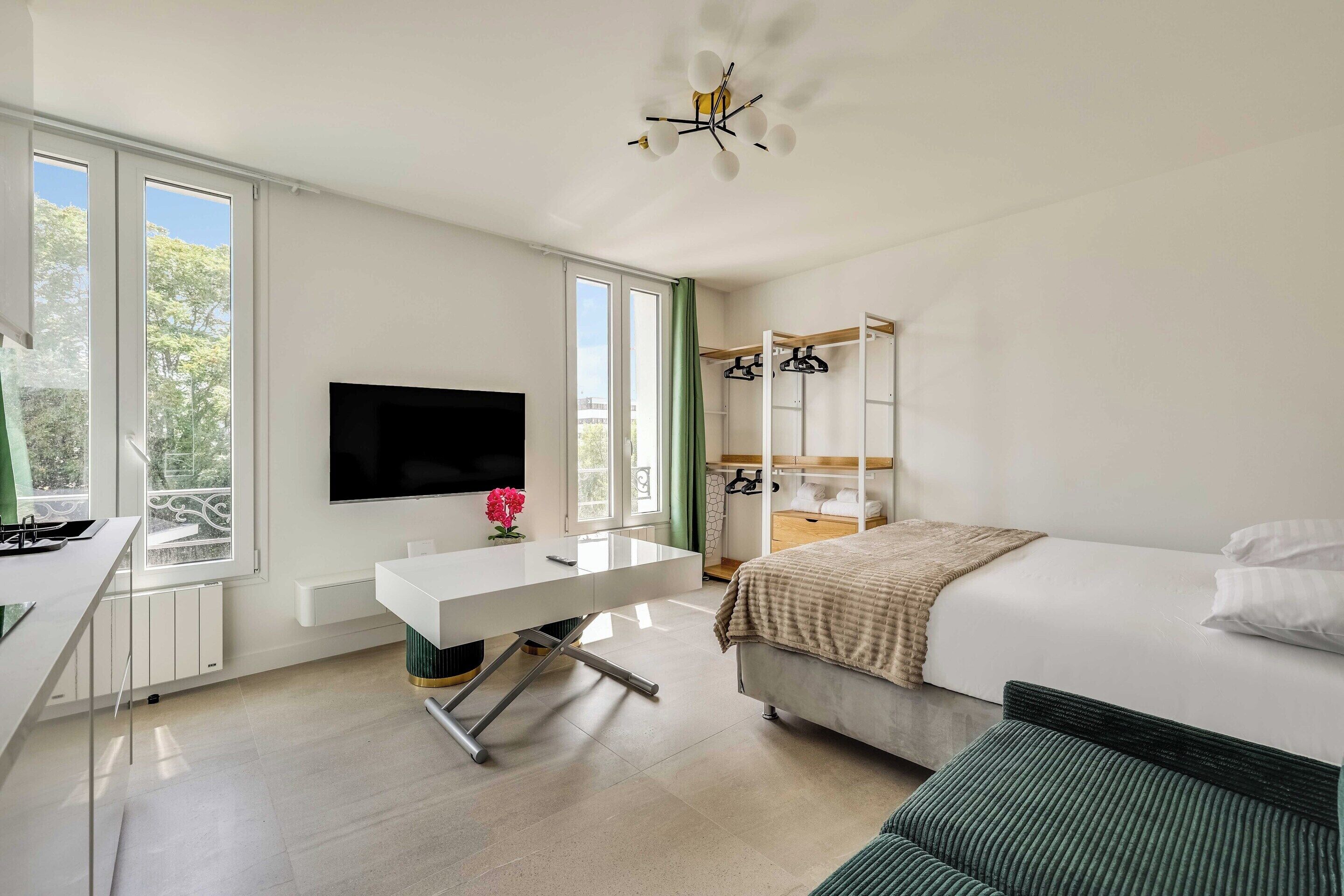 A modern bedroom with a bed, bedside table, TV, and a window with a view.