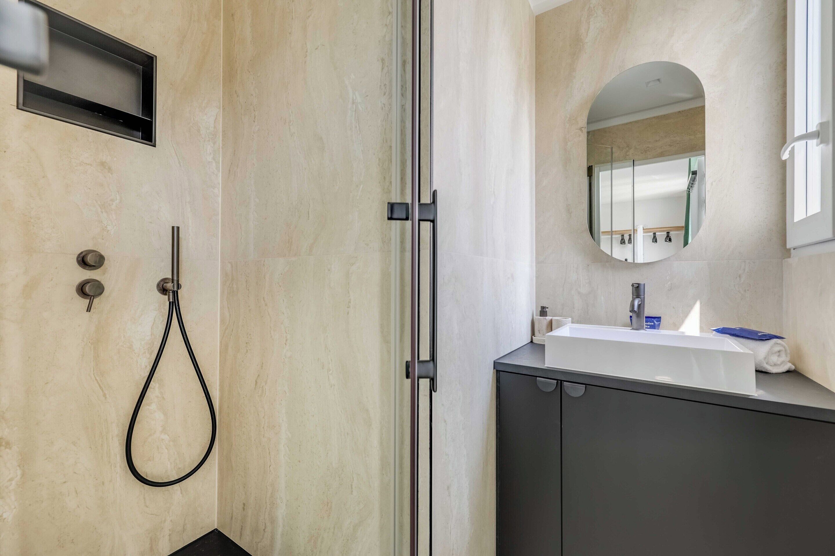 Een moderne badkamer met een douche, wastafel en spiegel.