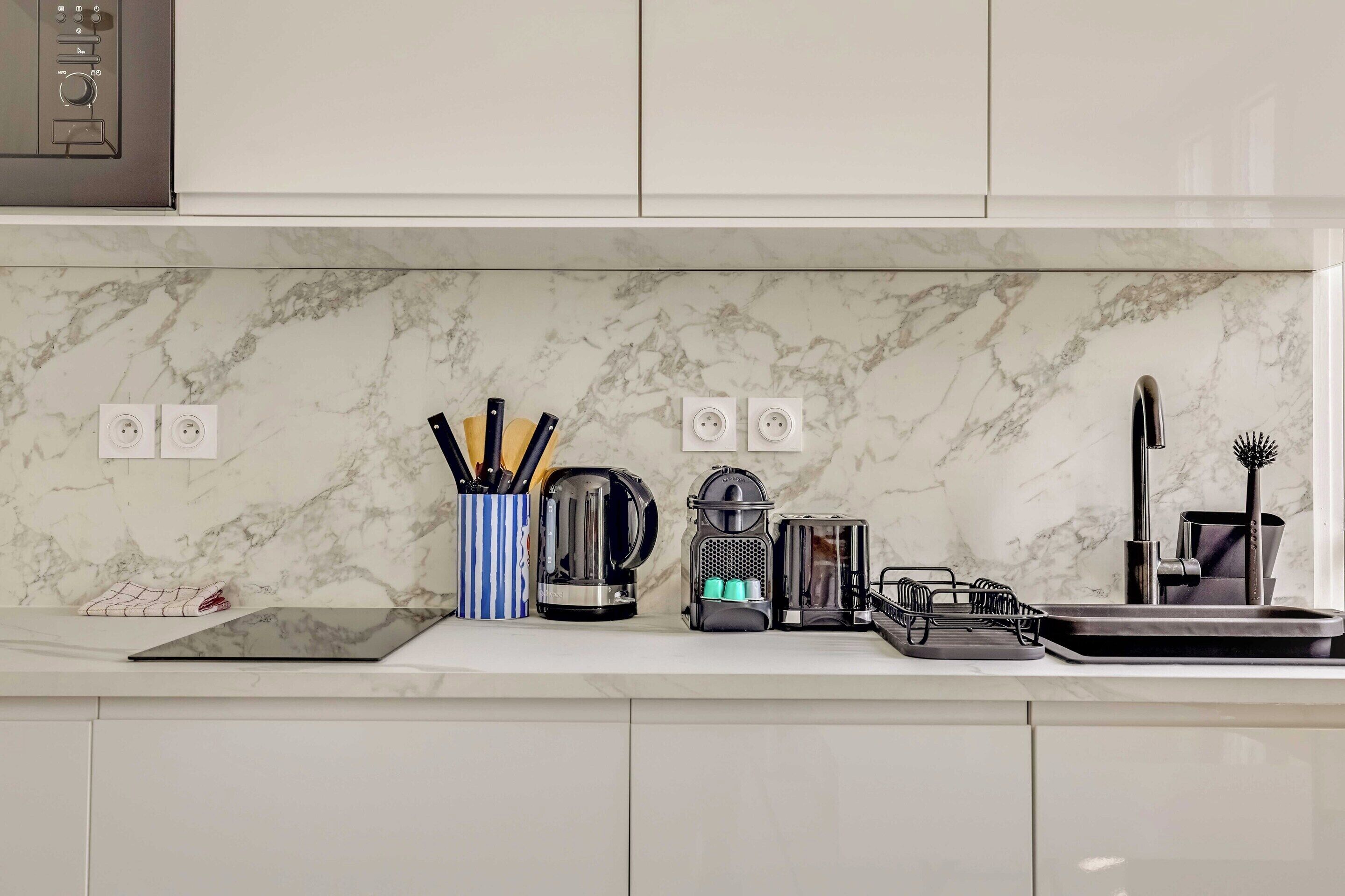 A kitchen with a marble countertop, a kettle, a toaster, and a sink.