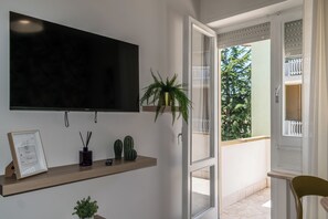 Ein modernes Zimmer mit Fernseher, einem Holzregal mit Dekoration, einer Topfpflanze und Blick ins Freie.