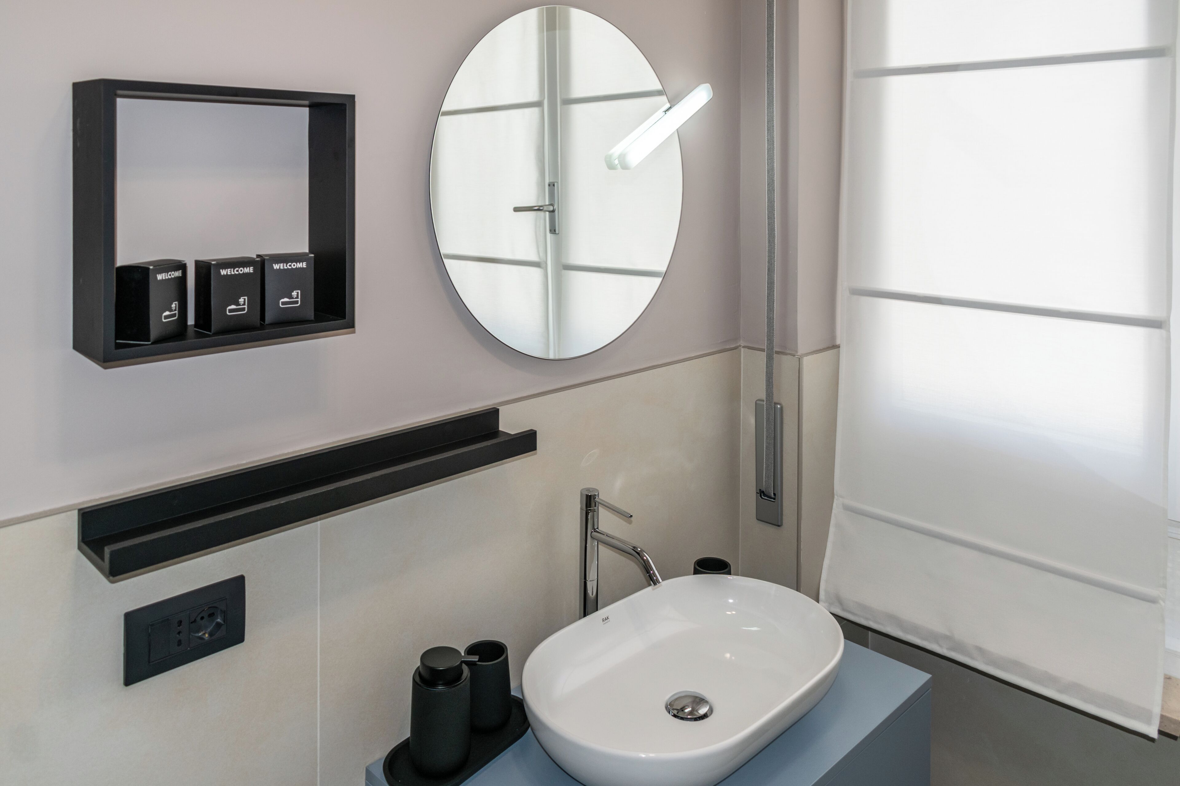 A modern bathroom with a round mirror, a white sink, a black medicine cabinet, and a towel rack.