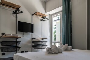 Ein Hotelzimmer mit Bett, Fernseher, Regalen und einem fenster mit Vorhängen.