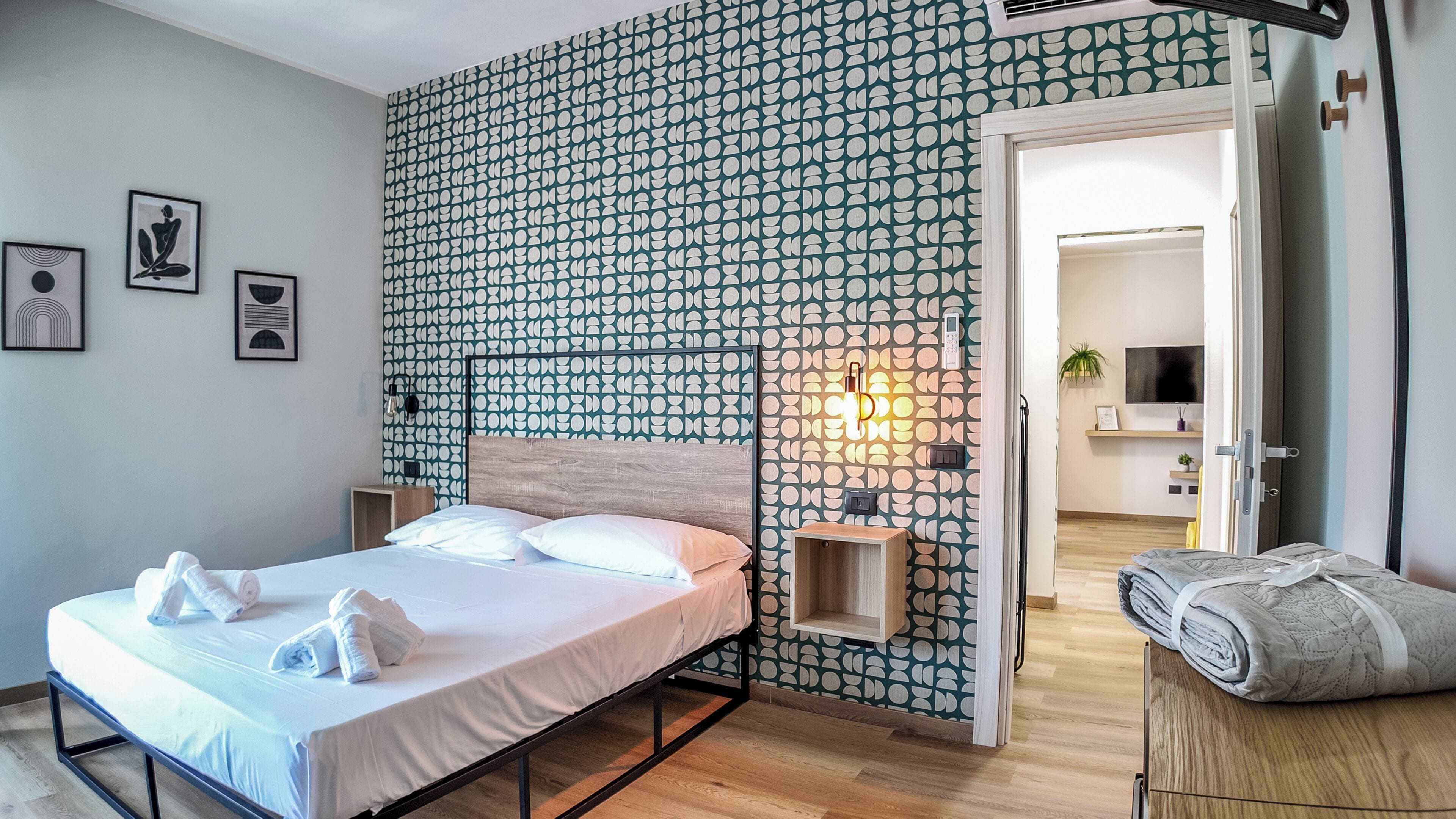 A hotel room with a bed, a bedside table, a wall-mounted phone, and a door leading to a bathroom.