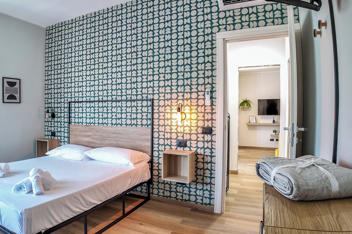 Una habitación de hotel con una cama, una mesita de noche, un teléfono en la pared y una puerta que da a un baño.