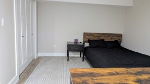 Ein Schlafzimmer mit Bett, Nachttisch, Holz-Kopfteil, einem gemusterten Teppich und einem Holztisch.
