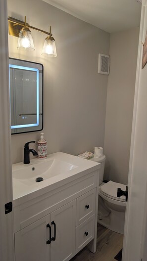 Ein Badezimmer mit weißem Waschtisch, einem Spiegel, einer Toilette und einer Duschkabine.