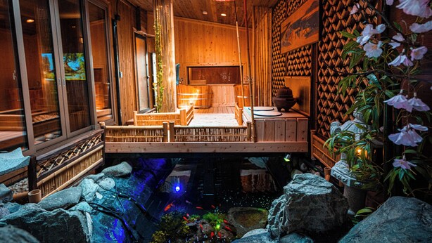 Um quarto tradicional japonês com piso de tatame, mesa de madeira baixa, porta deslizante e um pequeno jardim interno com pedras e um espelho d'água.