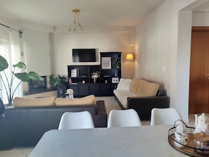 A modern living room with a sofa, chairs, a TV, and a dining table.