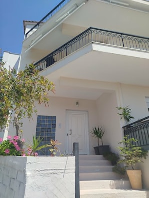A two-story building with a white facade, a balcony with black railings, and a door with a window above it.