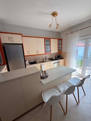 A modern kitchen with a central island, white bar stools, and a view to the outside.