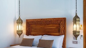 A bed with a wooden headboard, two wall-mounted lamps, and a bedside table with a digital device.