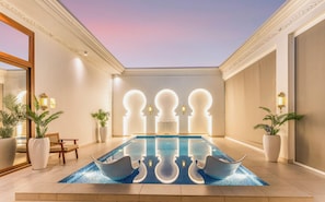 Una piscina moderna al chiuso con illuminazione a parete geometrica, piante in vaso e pavimento riflettente.