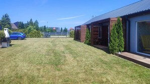 En bostadsfastighet med en välskött gräsmatta, en parkerad bil och ett modernt hus med ett stort fönster och en inglasad veranda.
