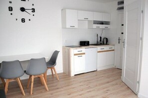 A compact kitchen with a clock, a dining area with chairs, and a white door.