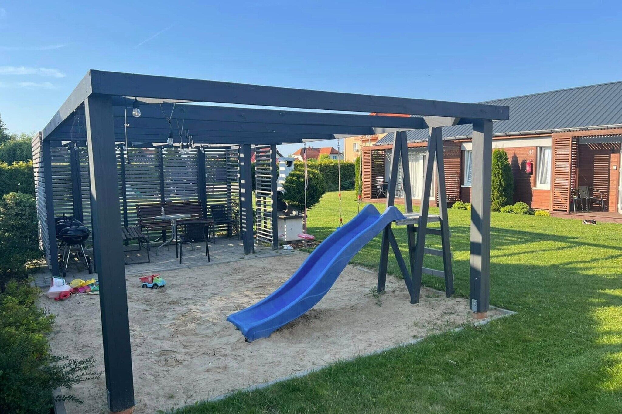Ein überdachter Spielbereich im Freien mit Rutsche, Sitzgelegenheiten und Grill.