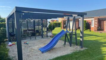 Un espace de jeux extérieur abrité, équipé d’un toboggan, de sièges et d’un barbecue.
