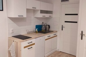 A compact kitchen with white cabinets, a sink, a kettle, and a countertop.