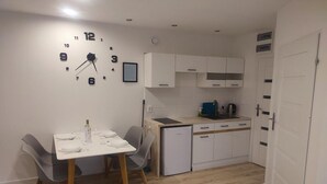 Ett kompakt kök med vita skåp, en inbyggd ugn och ett matbord med stolar.