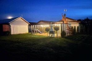 A residential property with a garage, a covered outdoor area with a slide, and a well-lit house at dusk.